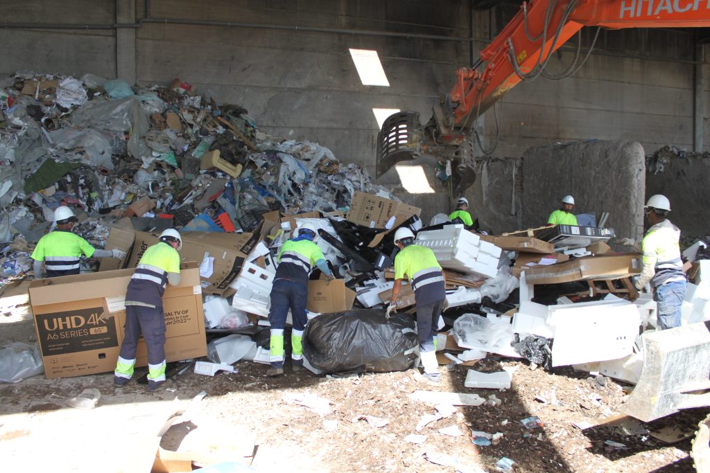 Trabajadores clasificando residuos junto a una excavadora